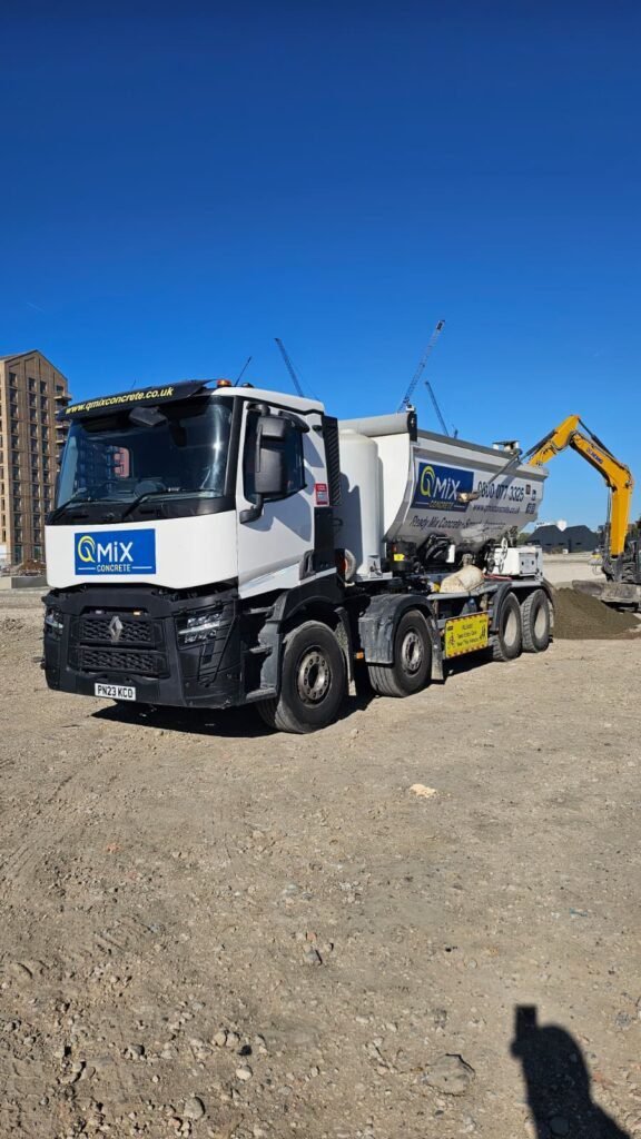 Lean Mix Concrete supplied by QMiX Concrete | QMiX Concrete White cement mixer truck on a construction site with a clear blue sky and cranes in the background.